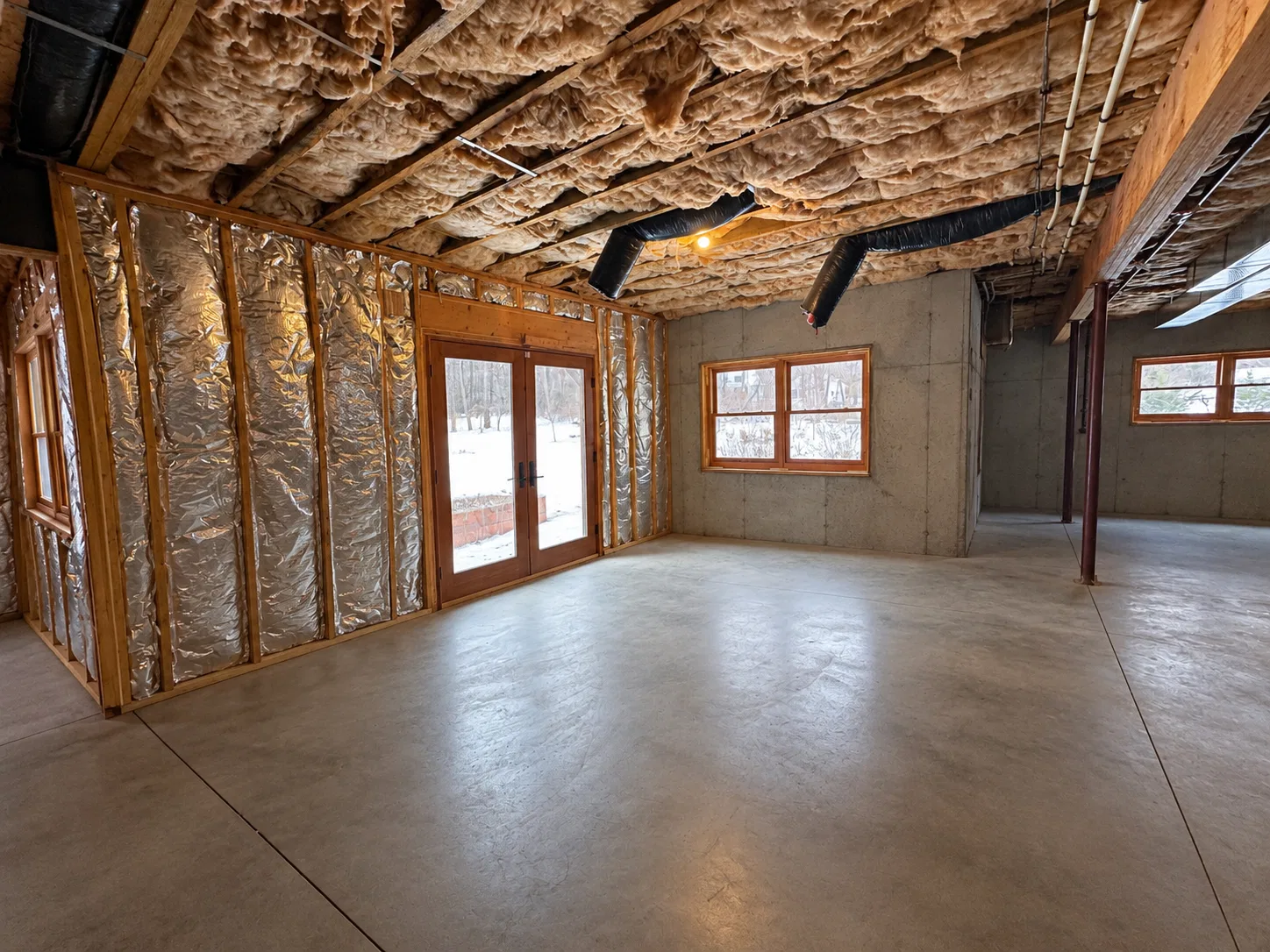 Before finishing: double glass exterior doors and wood-trimmed windows beside exposed basement wall insulation and a concrete floor.