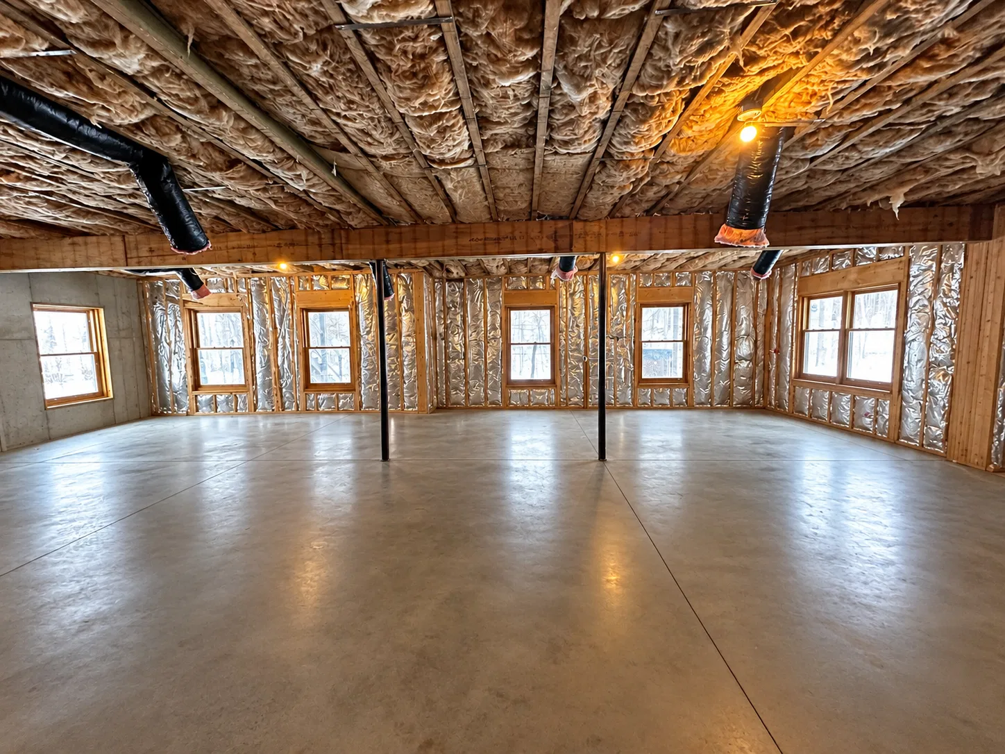 Before finishing: wide basement window wall with exposed framing and insulation, two steel posts and duct branches above a concrete floor.