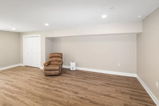 Brown recliner against a gray basement wall beneath recessed lighting, with wood-look flooring and a white door.