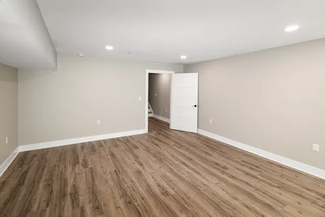 Finished basement corner with gray walls, white trim, wood-look flooring and an open white doorway.