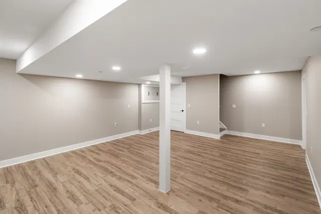 Open basement floor beneath a wide ceiling soffit and recessed lights, with a white support column.