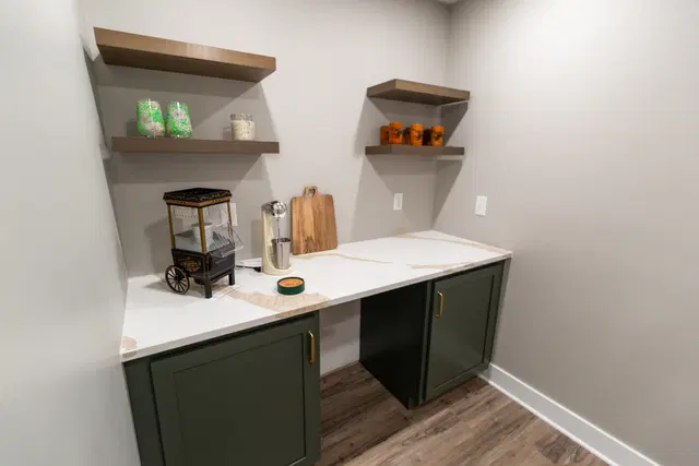 Coffee maker and floating wood shelves above a white counter, dark cabinets and a small refrigerator.