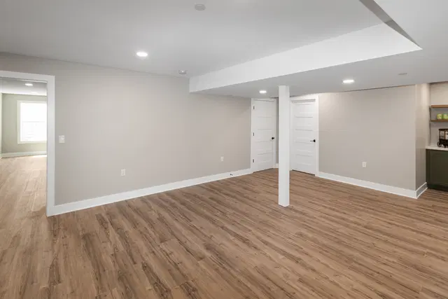 Open finished basement with gray walls, white trim, wood-look flooring and a support column under a ceiling soffit.