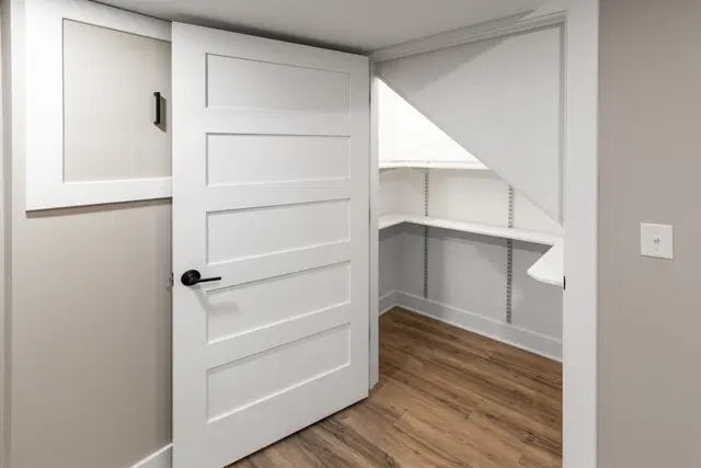 Under-stair storage closet with white shelves, a sloped ceiling and an open paneled door.