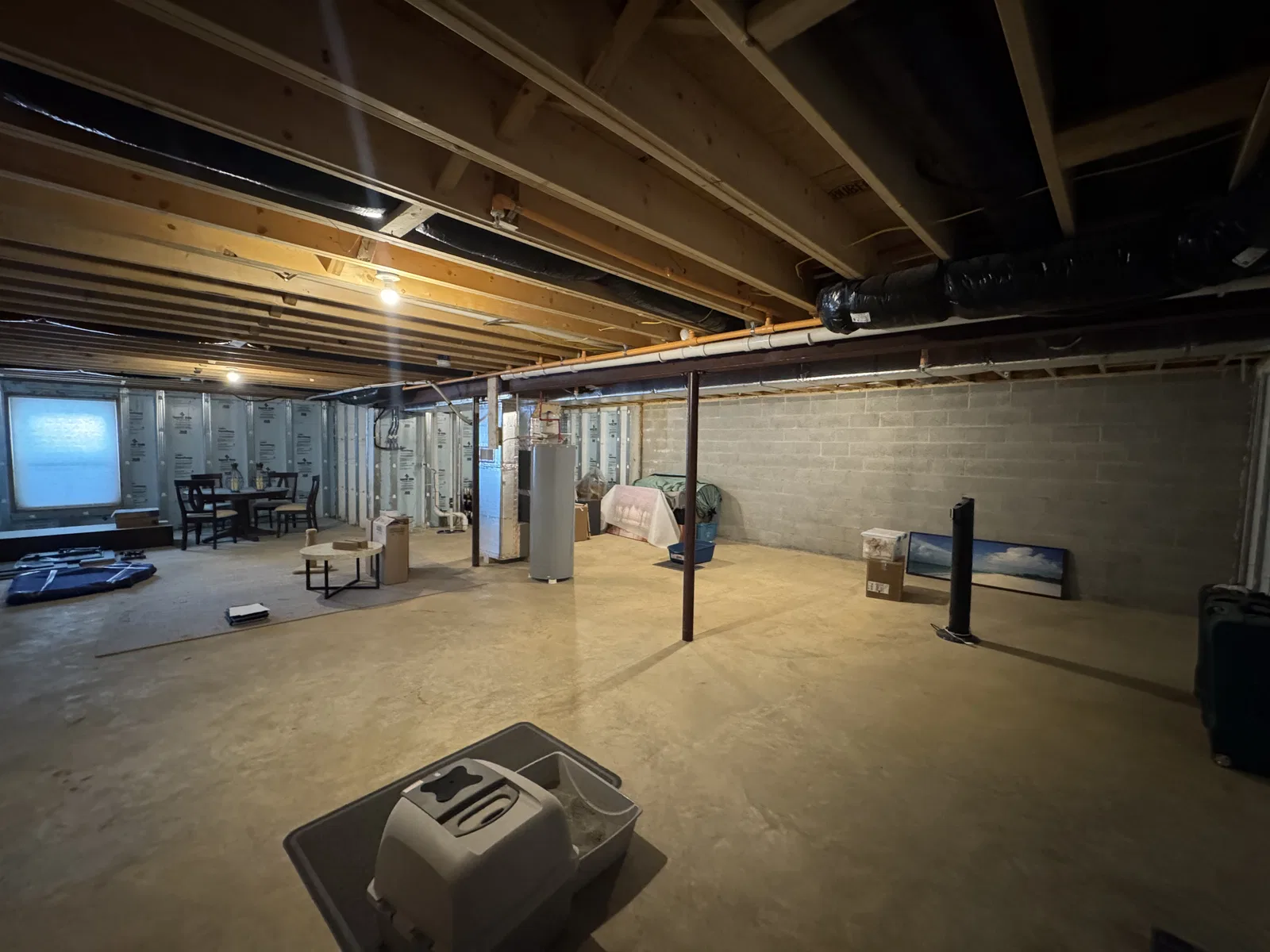 Before finishing: wide basement view with bare concrete flooring, exposed ceiling framing, block walls and steel support posts.