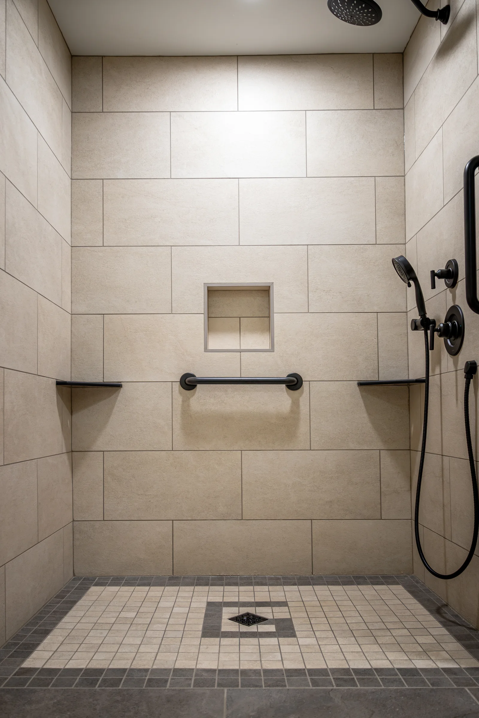 Walk-in shower with large beige wall tiles, a mosaic floor and black fixtures.