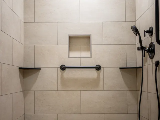 Walk-in shower with large beige wall tiles, a mosaic floor and black fixtures.