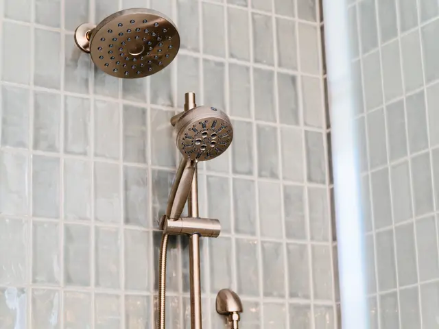 Round gold-tone rainfall showerhead and handheld spray against green rectangular wall tile.