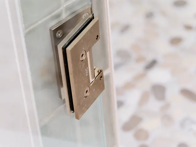 Close-up of a metal glass-door hinge beside the patterned shower floor.