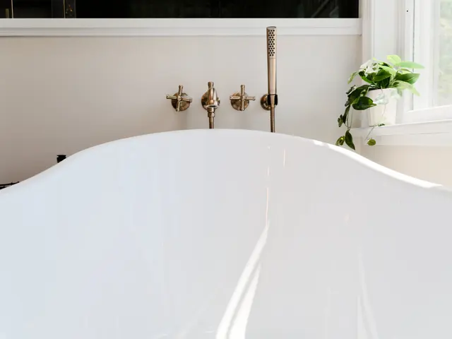 Curved rim of a white freestanding bathtub with wall-mounted gold-tone fixtures behind.