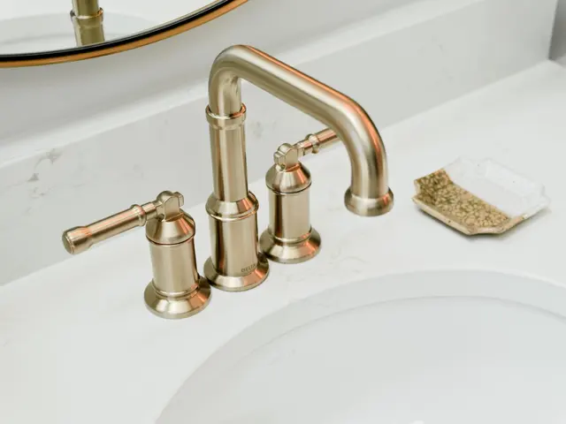 Close-up of a gold-tone bathroom faucet and cross handles on a white countertop.