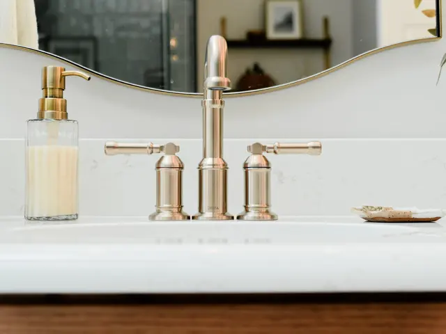Bathroom sink and gold-tone faucet beneath an arched mirror, with a soap dispenser beside it.