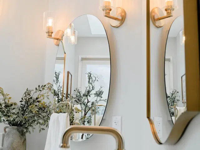 Gold-tone bathroom faucet beneath an arched mirror and glass-shaded wall lights.