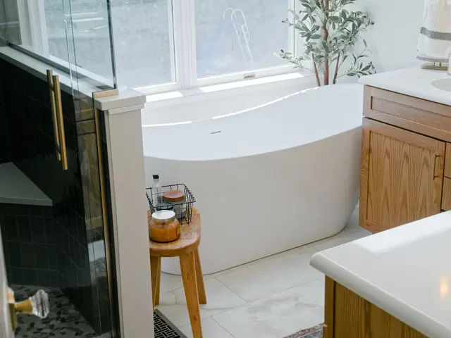 Freestanding bathtub beside the glass shower, with a wood vanity and a small side table.