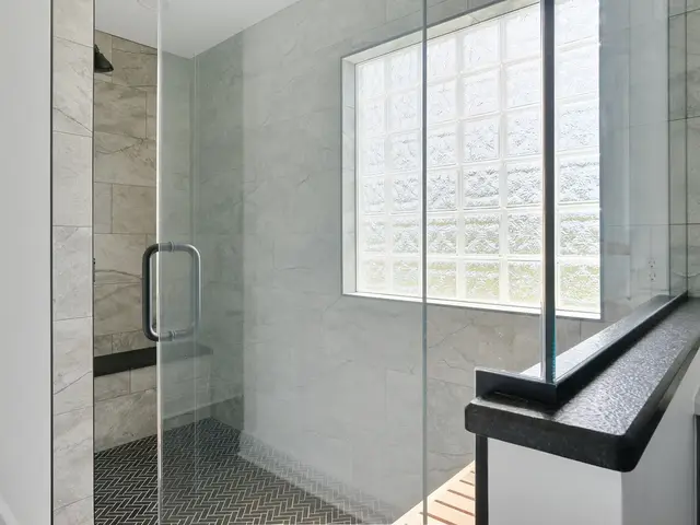 Glass shower with gray wall tile, black accent trim and a frosted glass-block window.