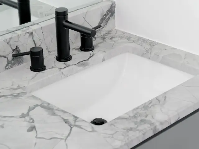 White undermount sink in a marble-look vanity countertop with a black widespread faucet.