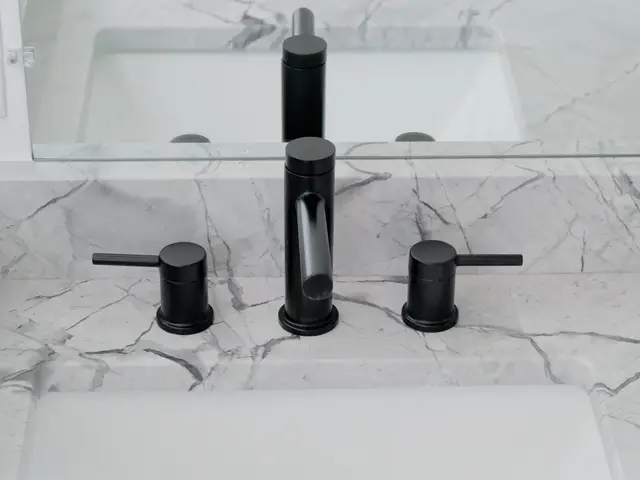 Front view of the matte-black vanity faucet and handles set into a veined countertop.