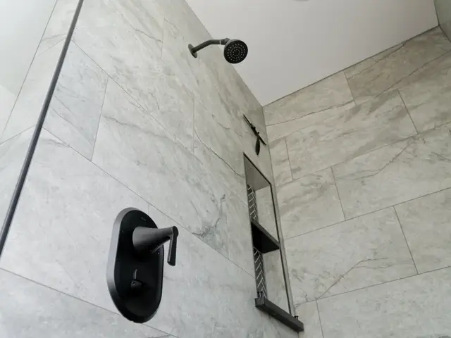 Black shower controls and handheld shower on a gray tiled wall.
