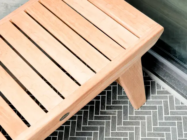 Wood shower bench beside the glass enclosure and dark herringbone floor tile.
