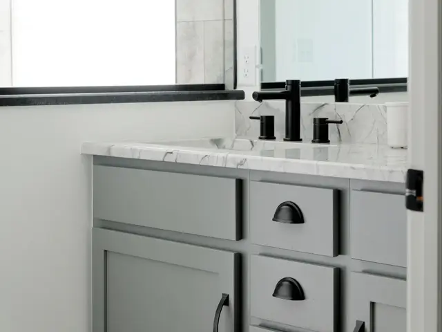 Gray vanity and black faucet beneath a black-framed mirror beside the shower.