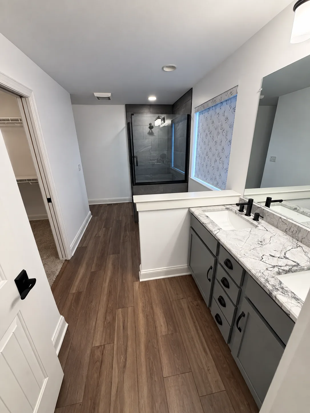 Before remodeling: Harrisburg bathroom with a gray double vanity, large mirror, built-in bathtub, dark-tiled shower and wood-look flooring.