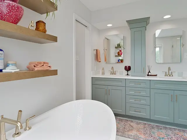 View across the bathtub toward a blue-green double vanity with a central storage tower and two mirrors.