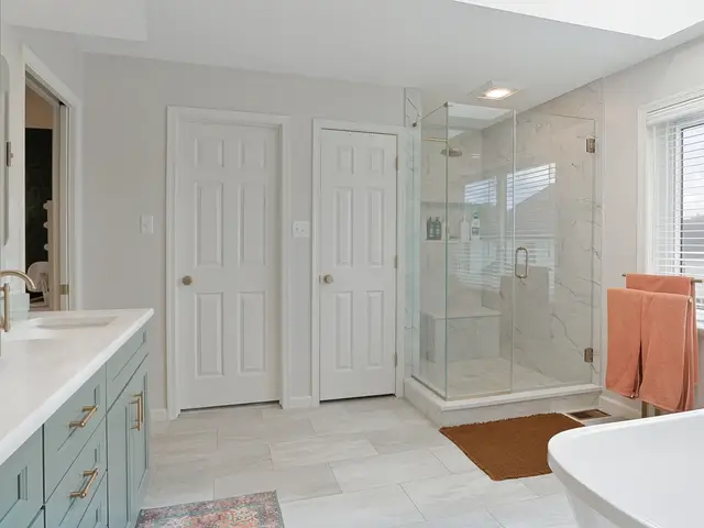 Wide view along the double vanity toward the glass shower, paneled doors and window.