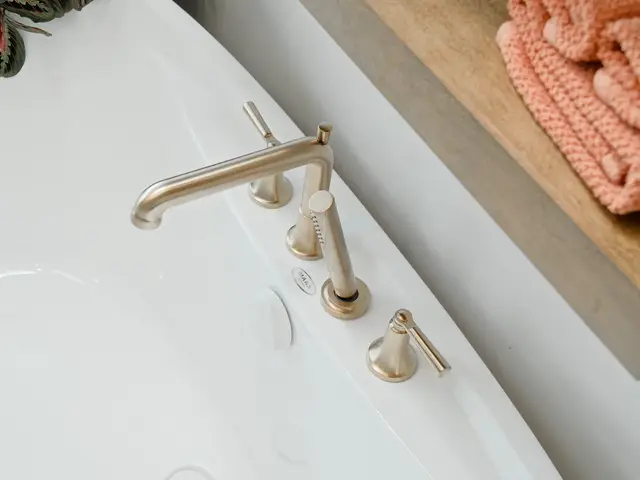 Overhead view of the gold-tone bathtub faucet and controls beside a wood shelf.