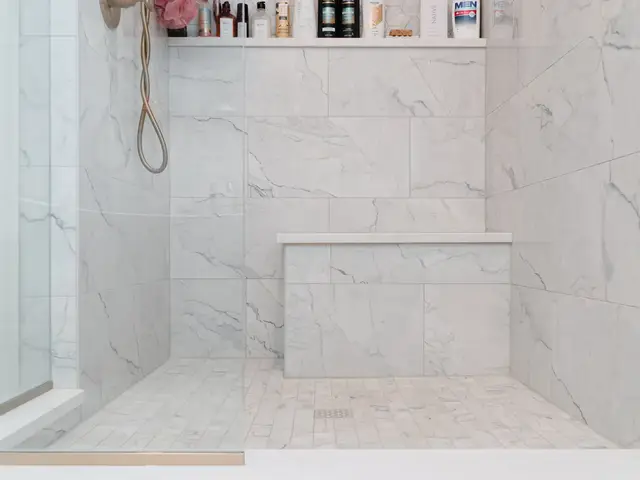 Marble-look tiled shower with a built-in bench, recessed niche and mosaic floor.