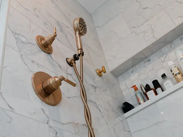 Gold-tone showerhead, handheld spray and controls against pale veined shower tile.