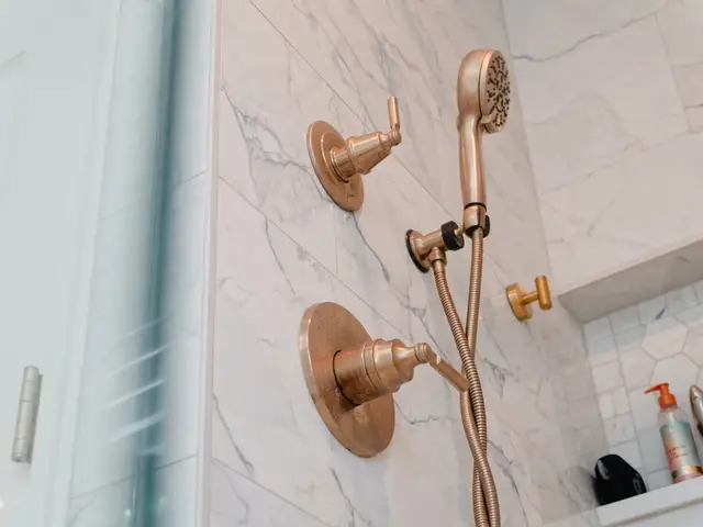 Gold-tone handheld shower and round controls beside the tiled storage niche.