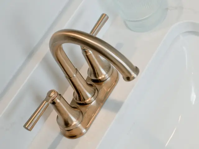 Angled close-up of a gold-tone vanity faucet beside a clear drinking glass.