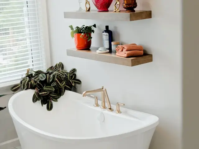 Freestanding tub beside floating wood shelves holding plants and colorful accessories.