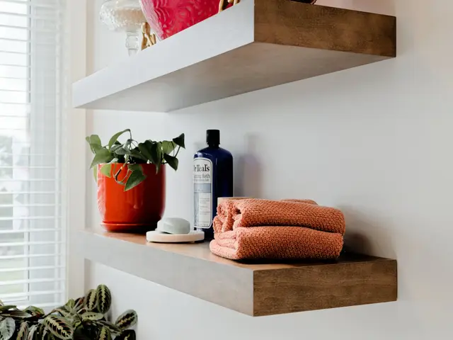 Close-up of floating wood shelves with a potted plant, bottles and folded orange towels.