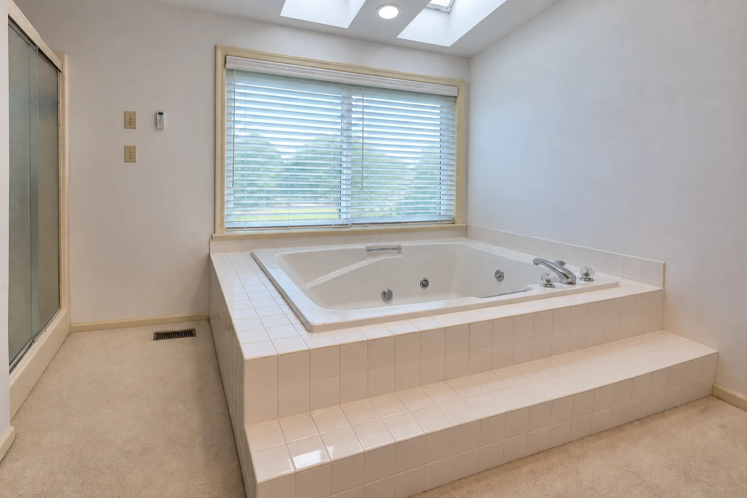 Before remodeling: Camp Hill bathroom with a built-in jetted tub, white tiled surround and step beneath a window, two skylights and beige carpet.