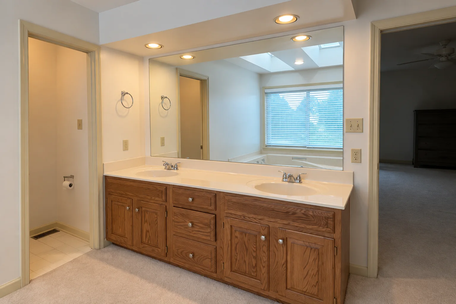 Before remodeling: oak double vanity with two sinks, a wide wall mirror and recessed lighting in the Camp Hill bathroom.