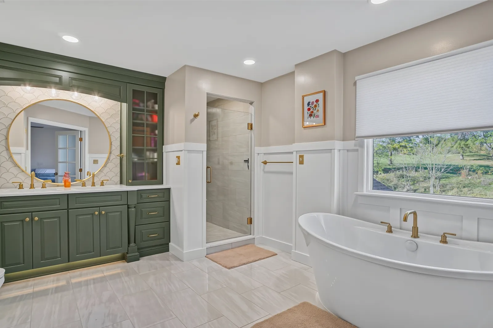Wide view of the finished bathroom with a freestanding tub beneath the window, sage green double vanity and glass shower.
