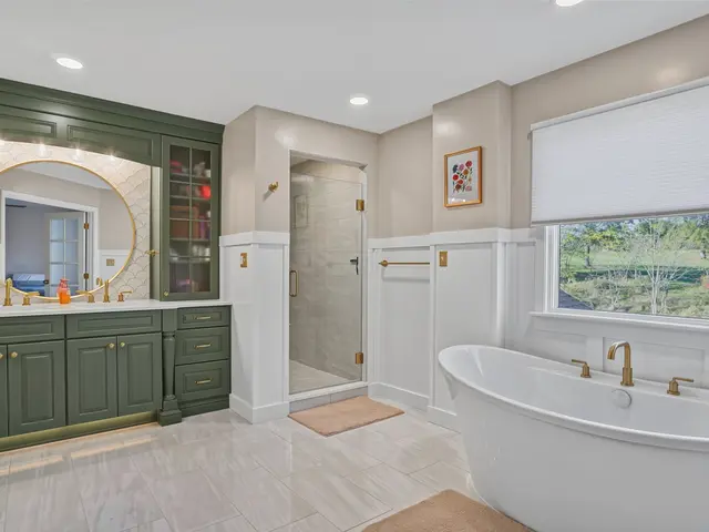 Wide view of the finished bathroom with a freestanding tub beneath the window, sage green double vanity and glass shower.