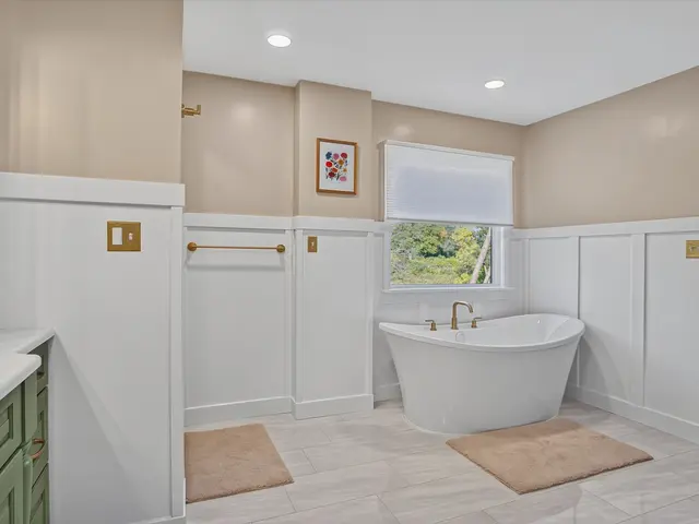 Wide view across the finished bathroom toward the window, freestanding tub and sage green vanity.