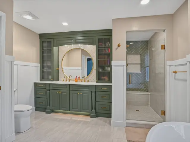 Finished bathroom seen from the doorway with a sage green vanity, round mirror and freestanding tub.