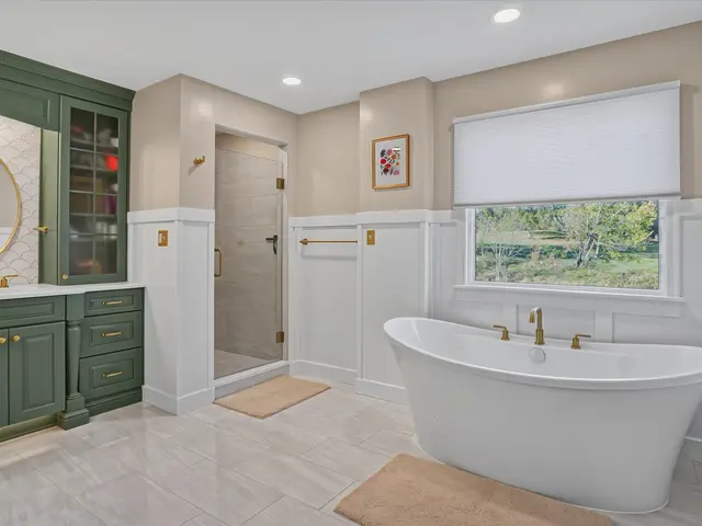 Wide view of the finished bathroom with a freestanding tub under the window and sage green vanity beside a glass shower.
