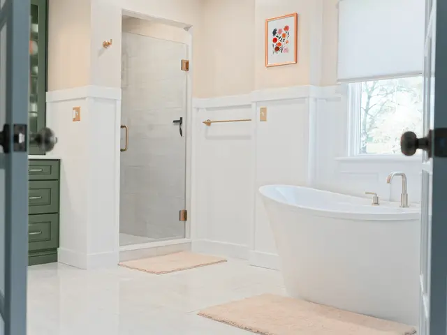Freestanding white tub beside open paneled doors, with the glass shower and a green cabinet in the background.