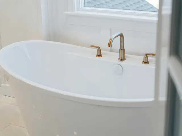 Curved white freestanding tub with a gold-tone deck-mounted faucet beside a window.