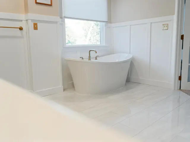 View along the bathroom wall toward a freestanding tub with a paneled door and window.