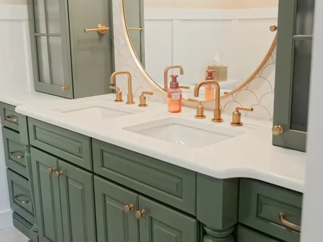 Sage green vanity cabinets beneath a white countertop with gold-tone faucet and an orange soap dispenser.