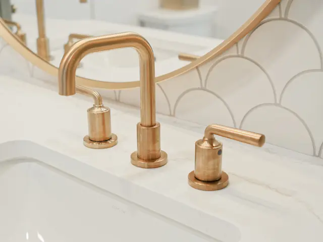 Close-up of a gold-tone widespread faucet and handles at the vanity sink with a gold-framed mirror.