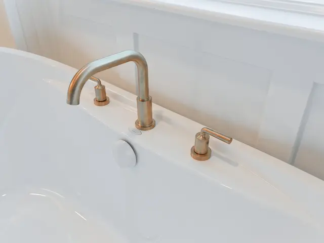 Close-up of a freestanding tub with a gold-tone faucet and handles beside the window.
