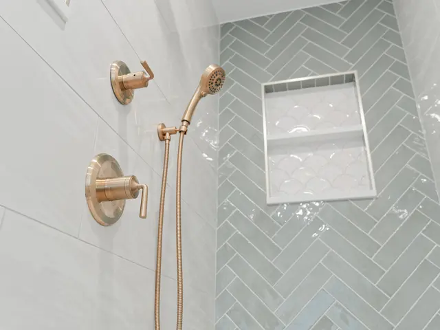 Gold-tone shower controls and handheld spray against white tile with a green herringbone niche.