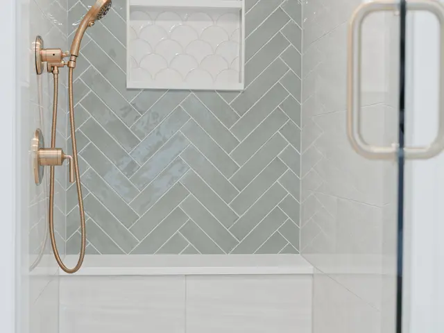 Glass shower with sage green herringbone tile, a recessed niche and a gold-tone handheld shower.