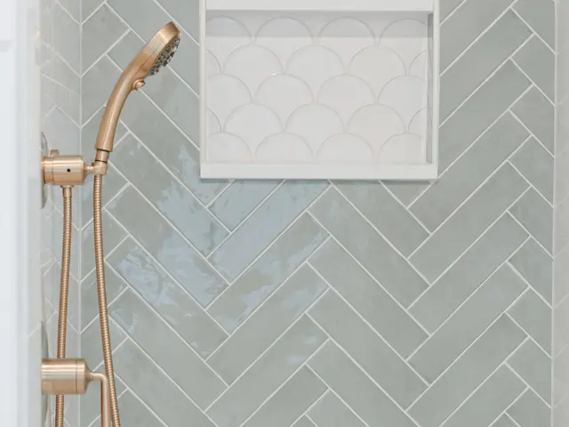 Vertical view of the shower niche in green herringbone tile with a brushed-gold handheld shower.